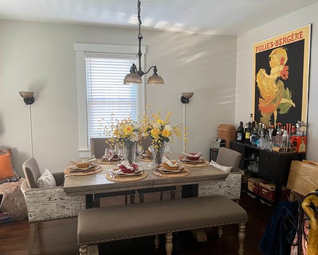The dining area features a large table set for a meal, adorned with flowers, alongside upholstered chairs and a vintage poster on the wall.