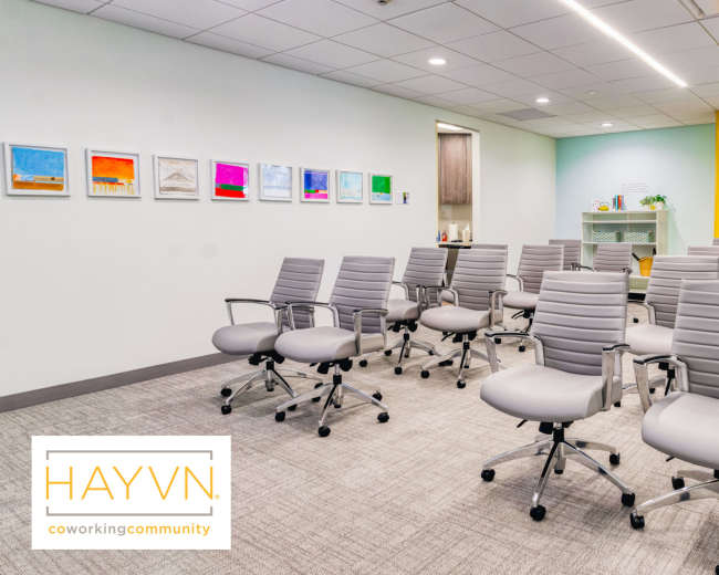The image shows a meeting room with several gray swivel chairs arranged in rows, complemented by colorful artwork on the walls and a light green and yellow interior design.