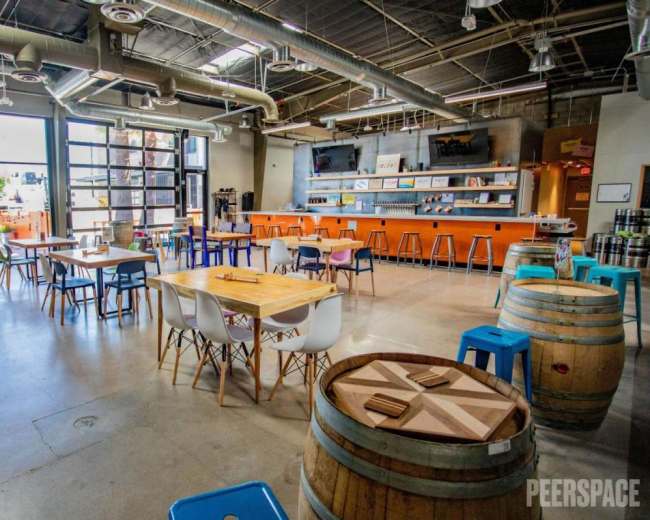 The image shows a spacious, modern indoor area with various tables, colorful chairs, and a bar counter along one wall.