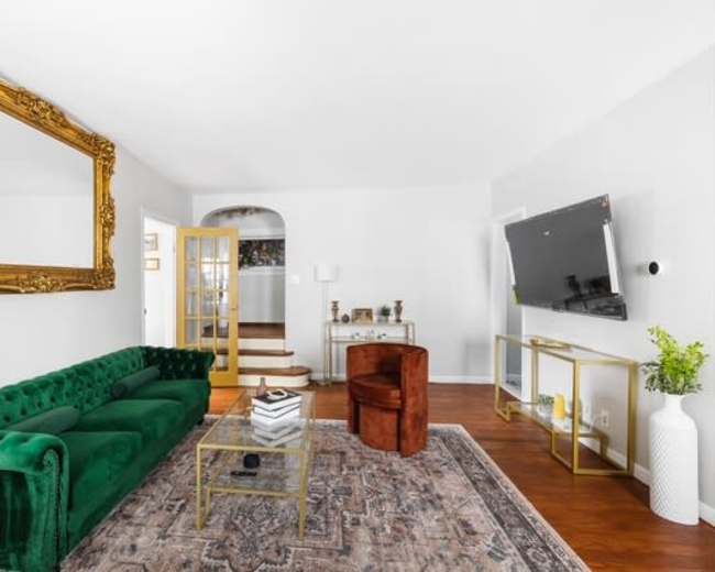 The image shows a modern living room featuring a green velvet sofa, an ornate gold mirror, and a flat-screen TV mounted on the wall.