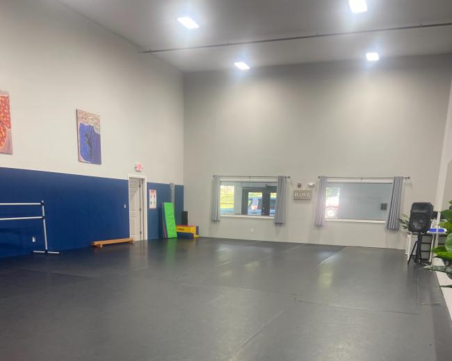 The image shows a spacious dance studio with a polished black floor, mirrors on one wall, and various exercise equipment along the sides.