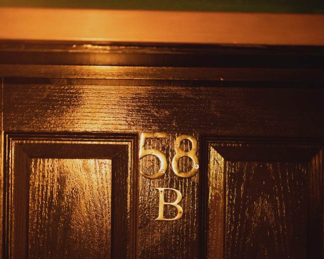 The image shows a dark wooden door with the number "58" and the letter "B" displayed prominently above a circular door knocker.