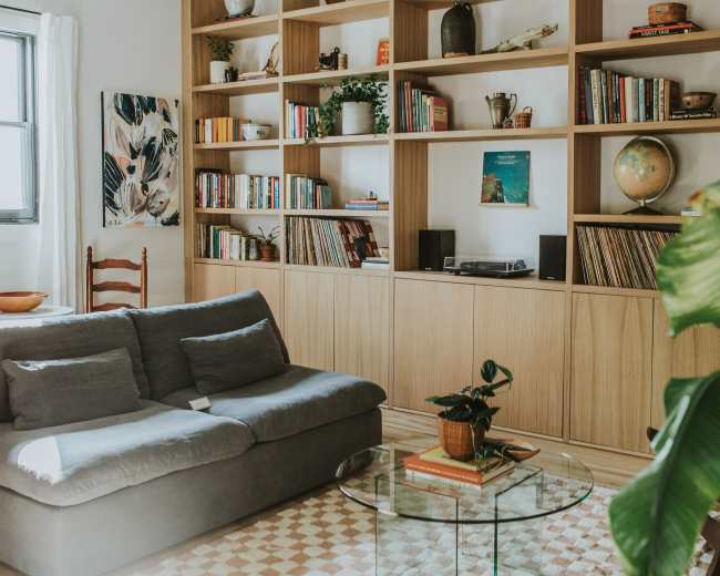 A cozy living room features a gray sofa, a glass coffee table, and a bookshelf filled with books and decorative items.