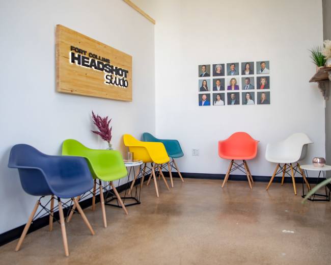 The image shows a waiting area with colorful chairs and a wall displaying framed portraits, alongside a sign for "Fort Collins Headshot Studio."