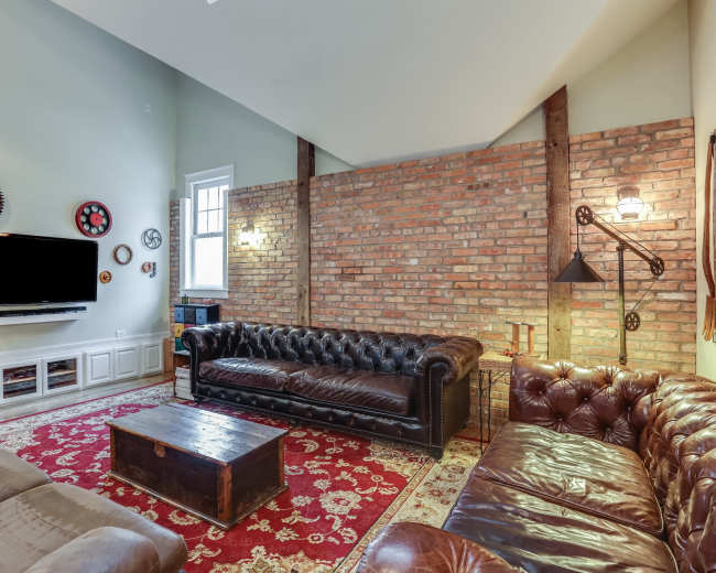 The living room features leather sofas, a coffee table, and a brick wall, creating a cozy atmosphere.