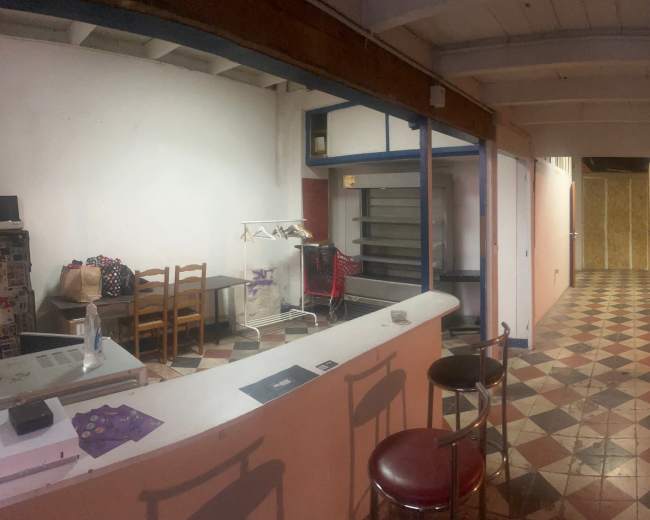 The image shows a spacious room divided into two areas, one featuring a bar counter and kitchen appliances, and the other containing a dining table and patterned tile floor.