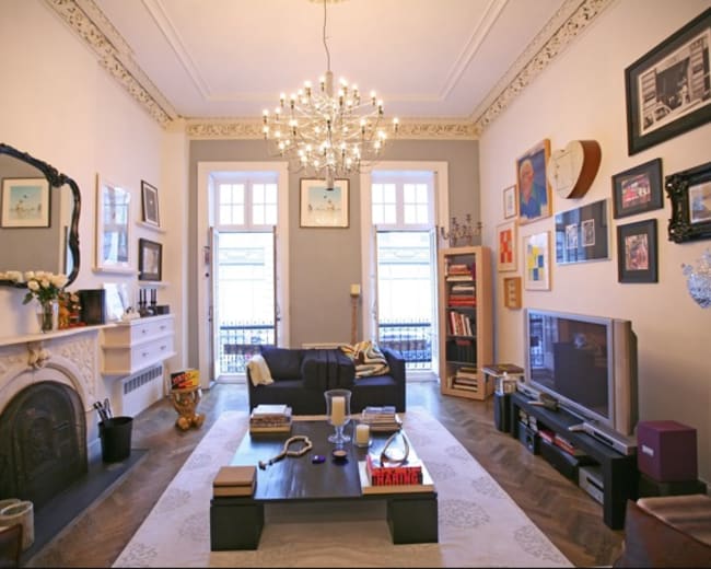 The living room features a chandelier, a dark sofa, a low coffee table, and an array of framed pictures on the walls.