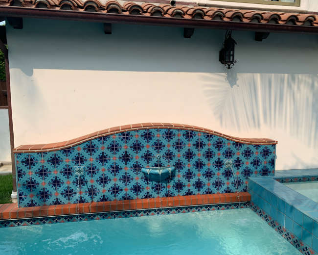 The image shows a decorative tiled fountain on a wall beside a swimming pool.