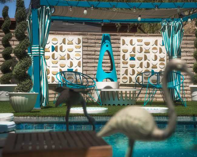 A backyard pool area features a turquoise canopy with seating, decorative topiaries, and flamingo sculptures beside a clear pool.