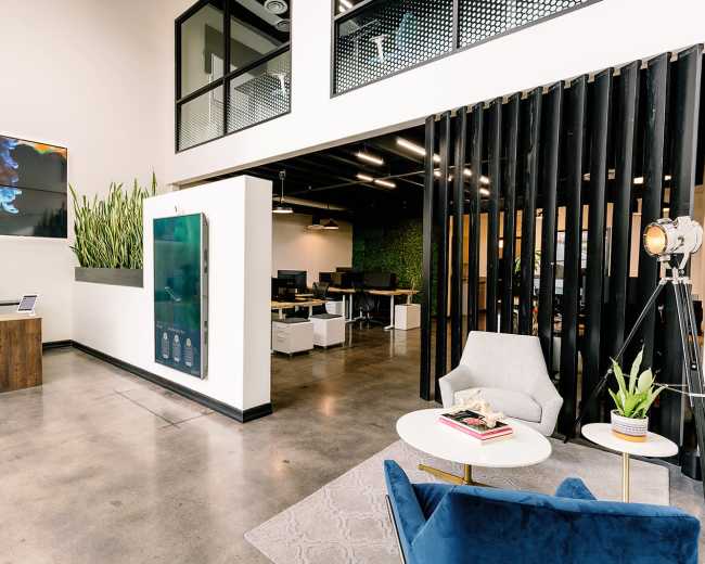 A modern office reception area featuring a large digital display, a wooden reception desk, and stylish seating arrangements with plants.