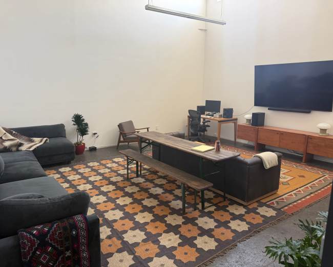 The image shows a spacious living room featuring a large gray sectional sofa, a long wooden coffee table, a wall-mounted TV, and a patterned rug on the floor.