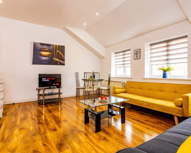 The image depicts a modern living room featuring a yellow sofa, a dark gray couch, a glass coffee table, and a television displaying a streaming service.
