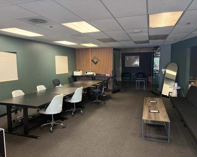 The image shows a modern conference room with a large table and chairs, a printer, and an adjacent seating area.