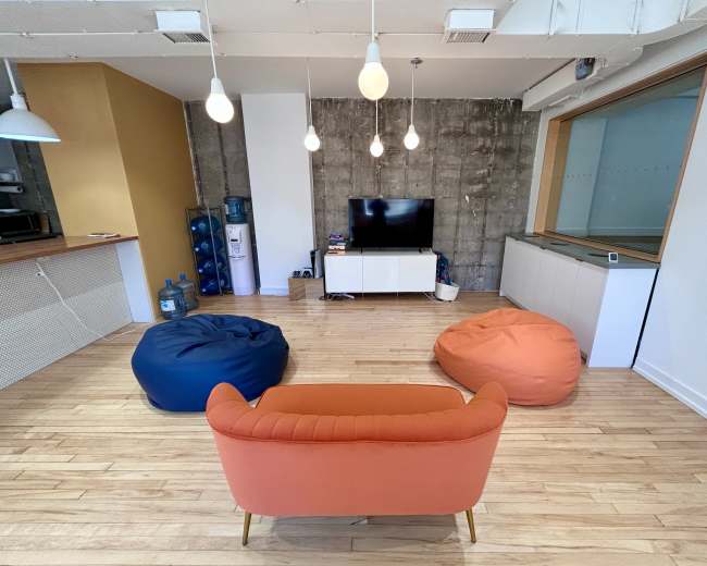 The image shows a modern living space featuring a television on a white media console with two colorful bean bag chairs and a coral couch arranged around it.
