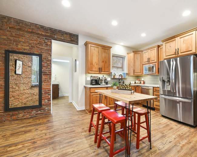 A modern kitchen features wooden cabinetry, stainless steel appliances, and a central island with red stools.