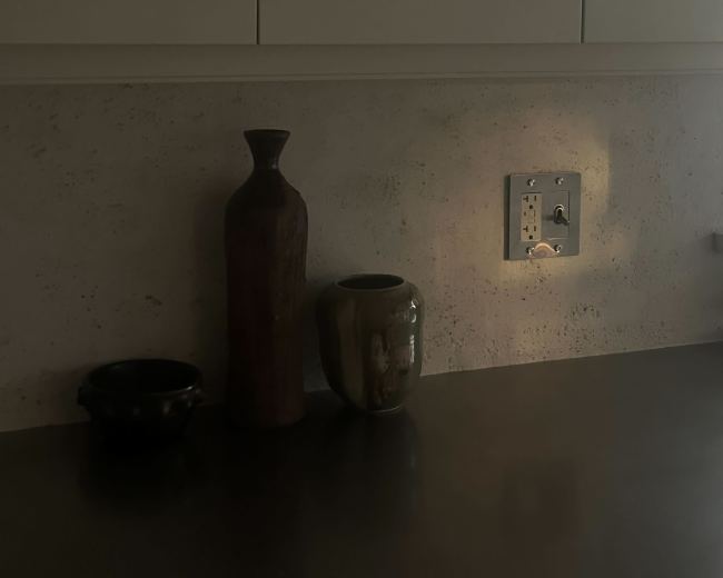 The image shows a kitchen counter with three vases and an electrical outlet against a textured wall.