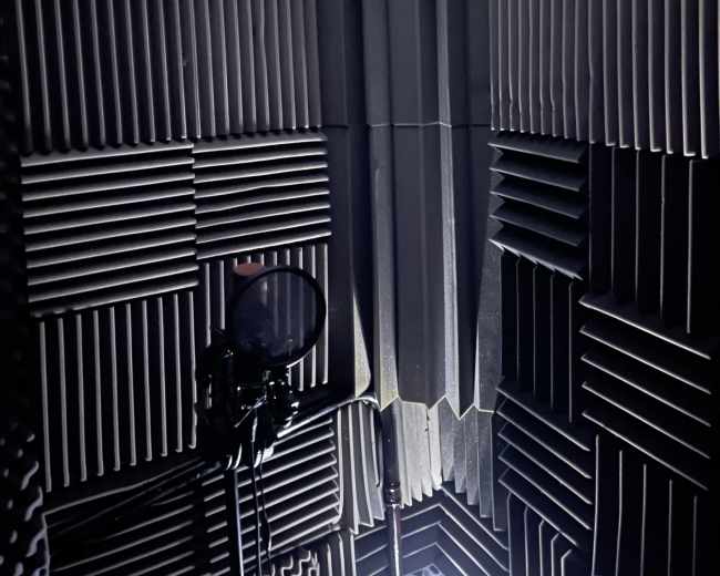 A corner of a soundproof studio, featuring acoustic foam panels and a microphone on a stand.