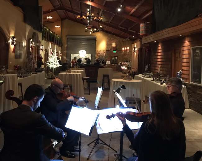 A string quartet performs in a warmly lit, elegantly decorated venue with tables arranged for an event.
