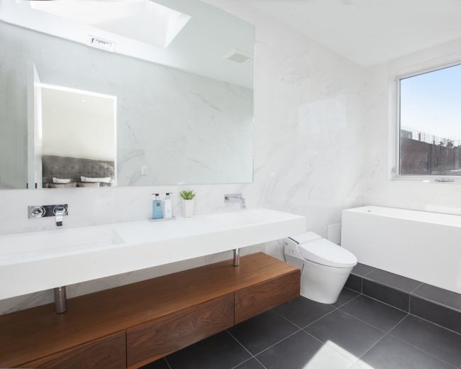 The image shows a modern bathroom with a large floating vanity, a freestanding bathtub, and a window providing natural light.