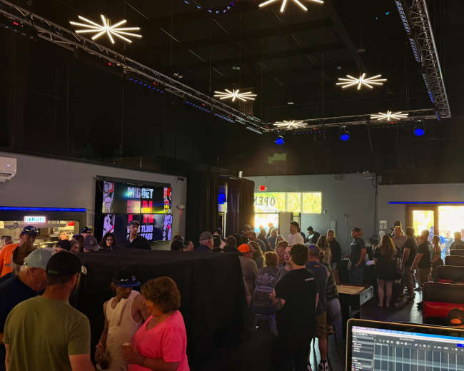 A crowded indoor venue features low seating areas and a bar, illuminated by star-shaped light fixtures.