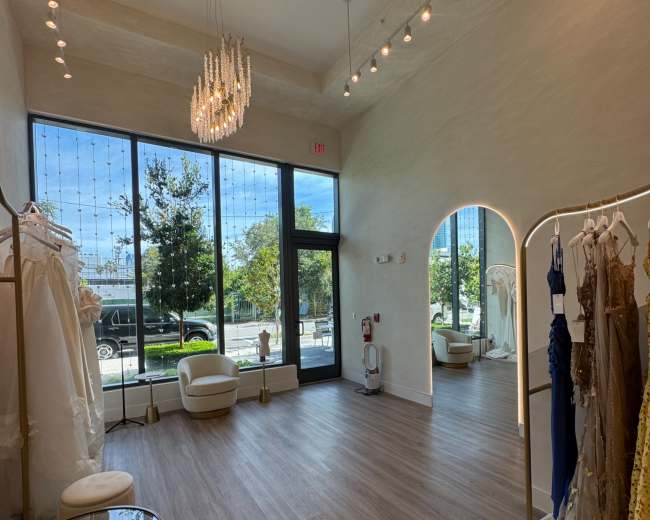 A bright bridal shop features elegant gowns displayed on racks, large windows allowing natural light in, and a modern seating area.