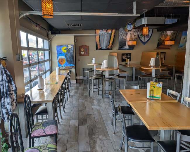 The image shows a modern restaurant interior with wooden tables, black chairs, and large windows that allow natural light, alongside decorative art on the walls.