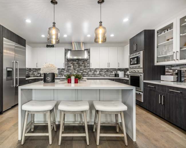 The image shows a modern kitchen featuring dark and light cabinetry, a large island with bar stools, and pendant lighting above.