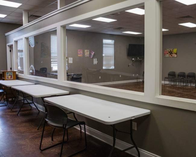 A room with a glass wall separating a seating area on one side from an empty meeting space on the other.