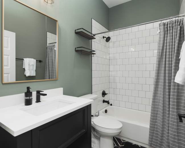 The image shows a modern bathroom featuring a white tiled shower area, a black vanity with a white sink, and gray patterned curtains.