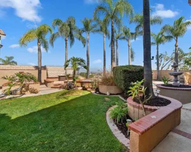 A landscaped yard featuring palm trees, garden beds, and a patio area with seating.