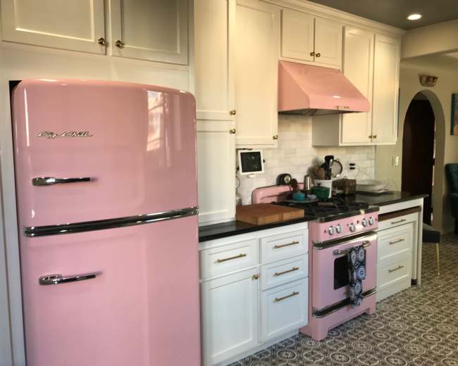 The kitchen features a pink retro-style refrigerator, matching pink range hood, and a black countertop with a stove and various kitchen appliances.