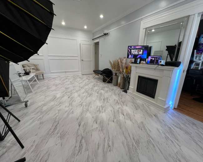 The image shows a well-lit room with a marble-patterned floor, a decorative fireplace, a large mirror, and photography equipment on one side.