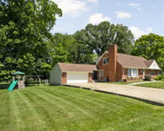 A brick house with a front lawn and a driveway, accompanied by a garage and a playground slide in the yard.