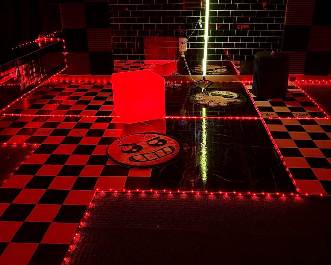 The image shows a room with a black and red checkerboard floor illuminated by red LED lights, featuring a large octopus decoration and various playful floor designs.