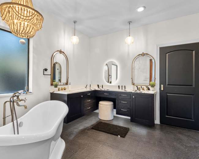 The image shows a modern bathroom featuring a freestanding bathtub, dual vanities with dark cabinetry, a chandelier, and large mirrors.