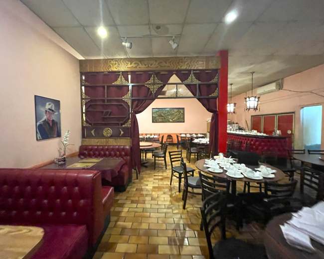 The image shows an empty restaurant interior with red booths, wooden tables, and a decorative divider, featuring a painting on the wall and white table settings.
