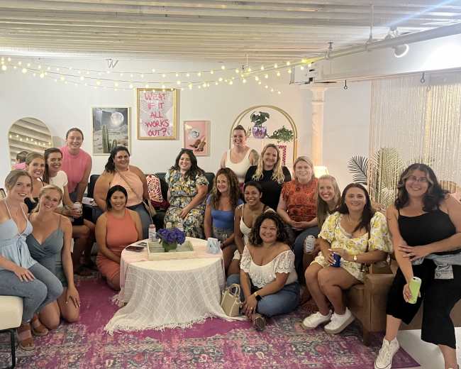 A group of diverse individuals poses together in a stylishly decorated room with string lights and colorful furnishings.