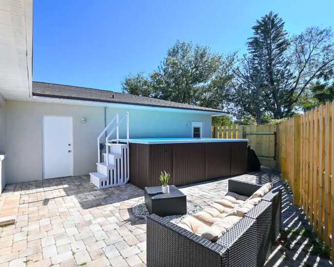 A patio area with a raised pool, surrounded by a wooden fence, and furnished with a wicker seating arrangement.