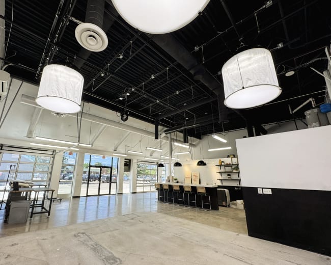 A spacious, modern office interior features large windows, industrial-style lighting, and a long counter with seating.