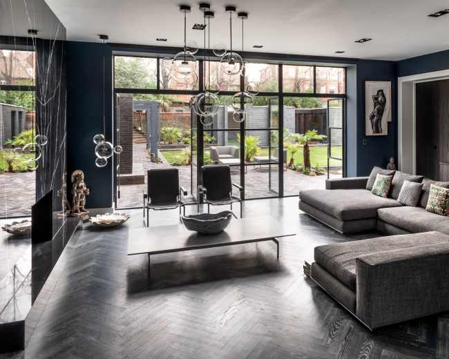 The image shows a modern living room with a sectional sofa, a coffee table, and large glass doors opening to a landscaped outdoor area.