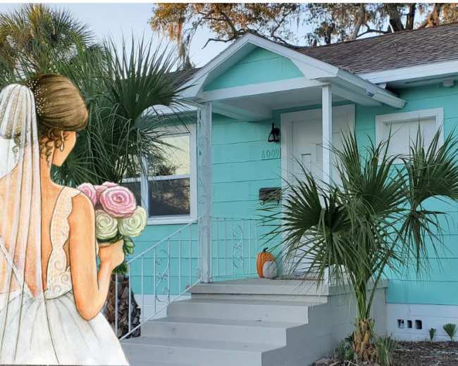 A bride holding a bouquet stands near the entrance of a turquoise house with palm trees in the front.