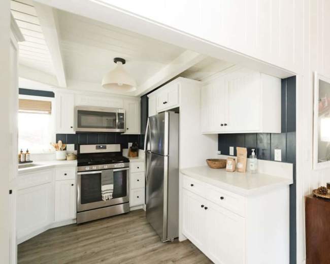 The image shows a modern kitchen with white wood cabinetry, stainless steel appliances, and a light-colored countertop.