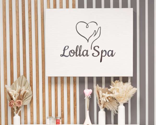 The image features a wall displaying a wooden sign with the logo of "Lolla Spa" above decorative vases and dried floral arrangements.