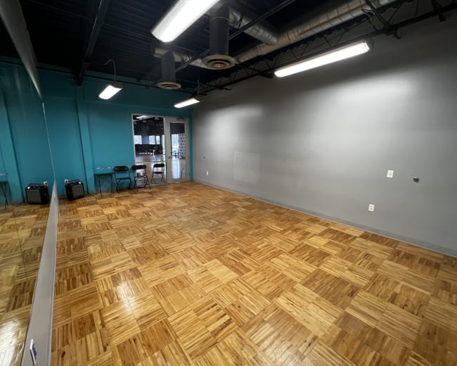 A spacious room with a hardwood floor, a large mirror on one wall, and doors leading to another area, all against a backdrop of teal and gray painted walls.