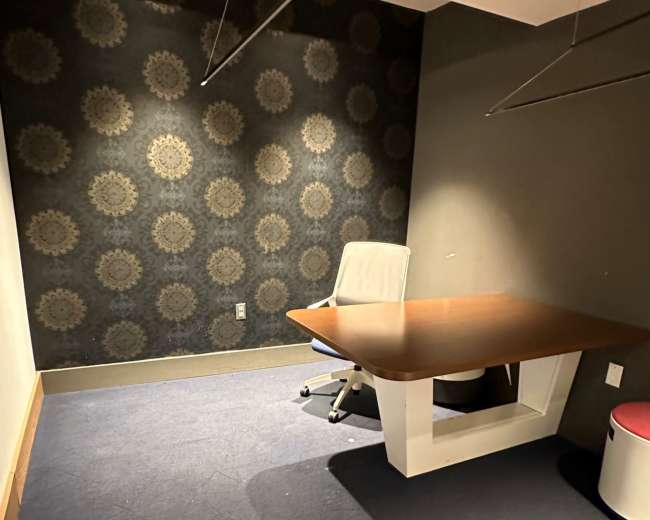 The image shows an empty office space featuring a desk, a chair, and patterned wallpaper on one wall.