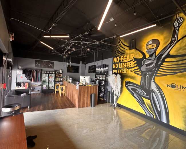 The image shows a fitness studio interior featuring a prominently painted mural of a woman in a superhero pose, a reception area with wooden counters, and shelves displaying merchandise.