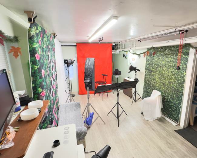 The image shows a small studio space with various backgrounds, including a floral and a green leafy pattern, along with lighting equipment and a photography setup in the center.