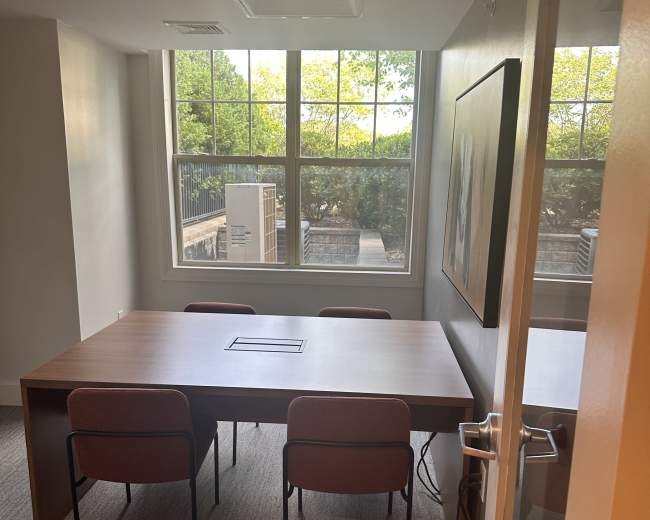 The image shows a conference room with a large table and four chairs, illuminated by natural light from a window.