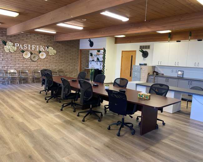 A spacious office with a long table, several black office chairs, and a decorative wall featuring the word "PASIFIKA."