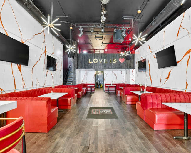 The image shows a restaurant interior with red booths, white tables, and decorative wall accents, including a "LOVE IS" sign and two televisions mounted on the walls.